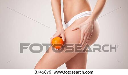 Stock Photo - Young woman holding an orange on the top of his thigh. Fotosearch