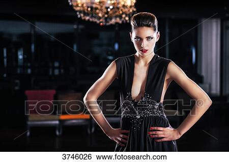 Stock Photograph - Young woman in evening dress, standing with hands on hips, looking toward the lens. Fotosearch