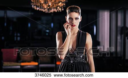 Stock Photography - Young woman in evening dress, standing with one hand on the cheek, looking toward the lens. Fotosearch