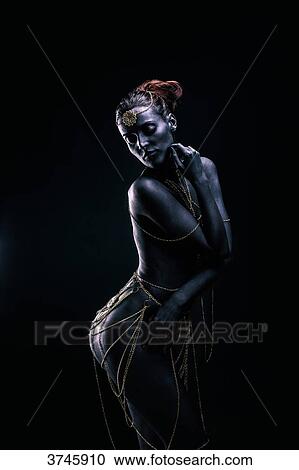 Stock Image - Young woman in light of ethnic ceremony, Length, Profile, a hand near the face, looking down. Fotosearch