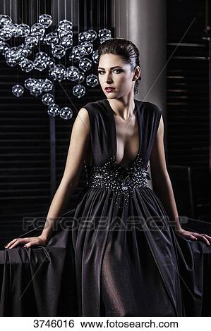 Stock Photograph - Young woman in profile evening dress, sitting, looking toward the lens. Fotosearch