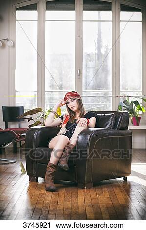Stock Image - Young woman in shorts, t-shirt and headband Sanhadja sitting on a leather chair. Fotosearch