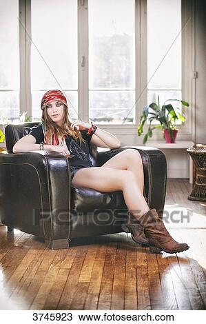 Stock Image - Young woman in shorts, t-shirt and headband Sanhadja sitting on a leather chair. Fotosearch