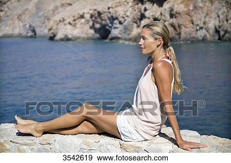 Young woman relaxing in the sun on a wall View Large Photo Image Stock Photo - Young woman relaxing in the sun on a wall. Fotosearch