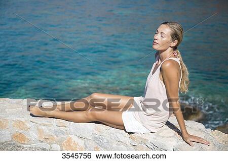 Young woman relaxing in the sun on a wall View Large Photo Image Stock Photograph - Young woman relaxing in the sun on a wall. Fotosearch