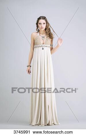 Stock Image - Young woman standing, front, wearing a beige dress Sanhadja. Fotosearch