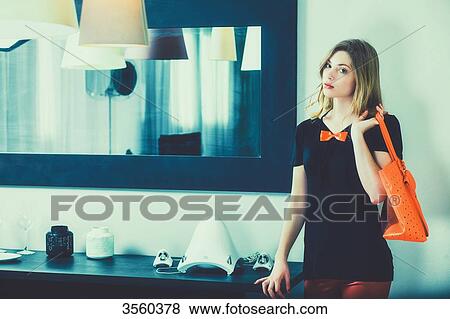 Stock Photo - Young woman standing holding her orange purse. Fotosearch