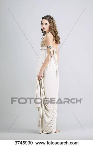 Stock Image - Young woman standing in profile, wearing a beige dress Sanhadja. Fotosearch