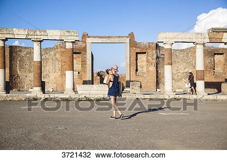 Stock Image - Young woman tourist, back, look at a map while walking in the ruins of Pompeii. Fotosearch