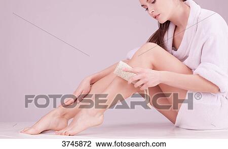 Stock Image - Young woman using a sponge massage on her leg. Fotosearch