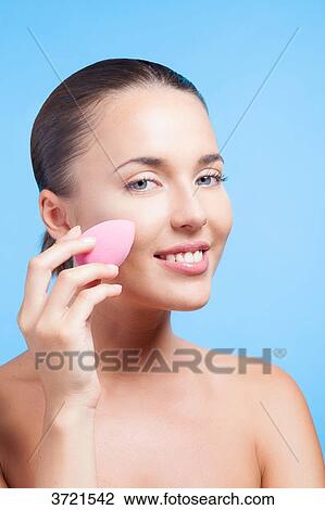Stock Image - Young woman using makeup sponge. Fotosearch