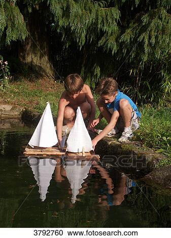 Stock Image - Boys playing with wooden boat in a pond. Fotosearch