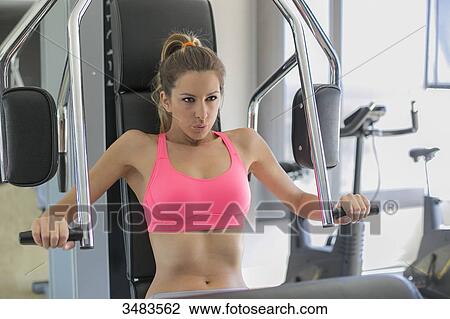 Stock Image - Concentrated athletic woman using a bench press in a fitness center. Fotosearch
