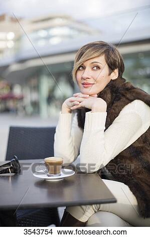 Picture - Daydreaming woman enjoying a coffee outdoors. Fotosearch