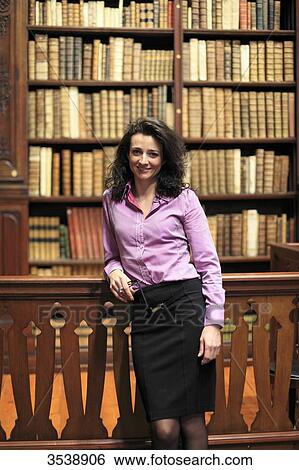 Elegant brown-haired young woman in a library with old books on the shelves. View Large Photo Image Stock Photograph - Elegant brown-haired young woman in a library with old books on the shelves.. Fotosearch