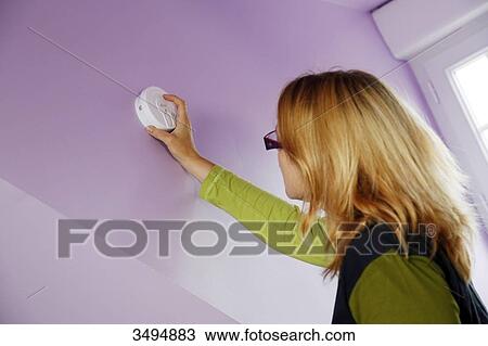 Stock Image - France, around Paris, 42 year old woman installing a smoke detector.. Fotosearch
