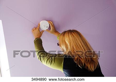 Stock Image - France, around Paris, 42 year old woman in the process of installing the ceiling smoke detector.. Fotosearch