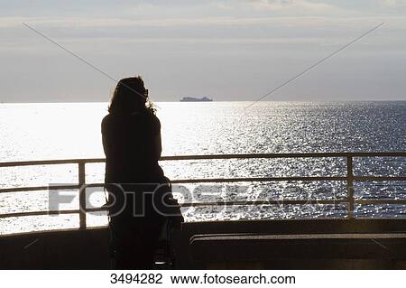 Stock Image - France, North-Western France, Saint-Michel-Chef-Chef, Tharon-Plage, young woman seen from behind, looking at the sea. Fotosearch