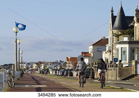 Stock Photography - France, North-Western France, Saint-Michel-Chef-Chef, Tharon-Plage, young people riding bikes on the bicycle path along the sea in the evening. Fotosearch