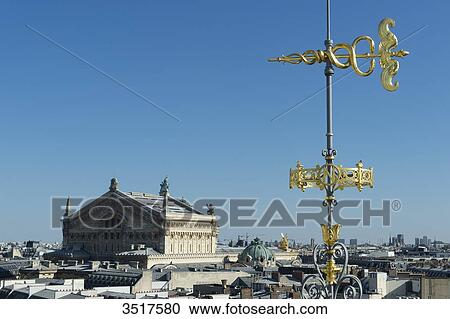 Stock Image - France. Paris 9th district. Weather vane of the terrace of the department store Au Printemps. Background: the Garnier Opera. Fotosearch