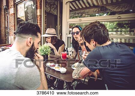 Group of young hipster sitting in a restaurant terrace, eating and drinking View Large Photo Image Stock Image - Group of young hipster sitting in a restaurant terrace, eating and drinking. Fotosearch