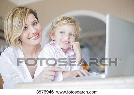 Mother and son with laptop at home smiling at camera View Large Photo Image Stock Photograph - Mother and son with laptop at home smiling at camera. Fotosearch