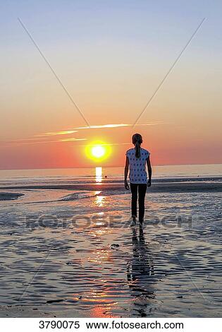 Stock Photography - Normandy, young girl seen from behind walking in the sun on a beach. Fotosearch