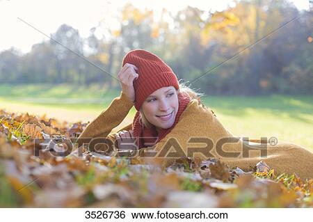 Stock Photograph - Pensive blonde woman lying in park in autumn. Fotosearch