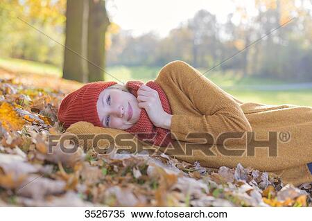 Stock Photography - Pensive blonde woman lying in park in autumn. Fotosearch