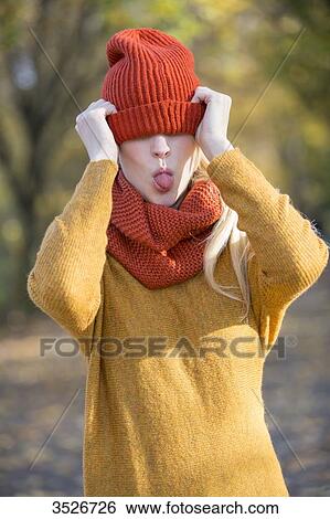 Playful young woman covering her eyes with cap in park in autumn View Large Photo Image Stock Photograph - Playful young woman covering her eyes with cap in park in autumn. Fotosearch
