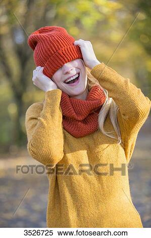 Playful young woman covering her eyes with cap in park in autumn View Large Photo Image Stock Photography - Playful young woman covering her eyes with cap in park in autumn. Fotosearch