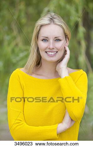 Stock Image - Portrait of a blonde woman in park smiling at camera. Fotosearch
