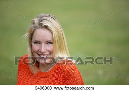 Stock Image - Portrait of a blonde woman sitting in the park and smiling at camera. Fotosearch
