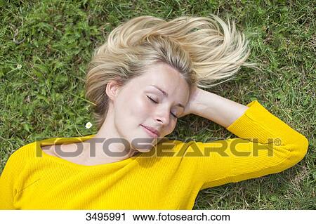 Stock Image - Portrait of a pretty blond woman lying down in the park with closed eyes. Fotosearch
