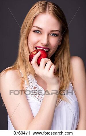 Stock Image - Portrait of a smiling young woman biting into an apple. Fotosearch