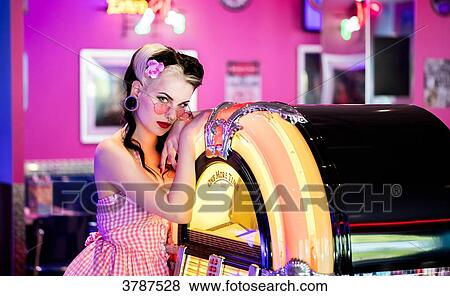 Stock Photo - Portrait of a young Pin Up, listening to music from a jukebox, looking toward the lens. Fotosearch