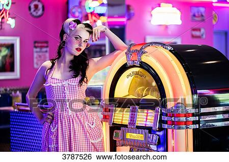 Stock Photograph - Portrait of a young Pin Up, listening to music from a jukebox, looking toward the lens. Fotosearch