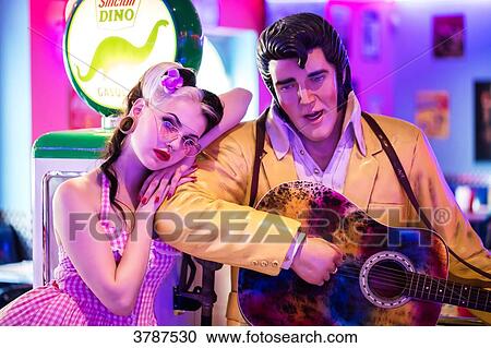 Stock Image - Portrait of a young Pin Up, resting on the shoulder of the statue of Elvis Presley. Fotosearch