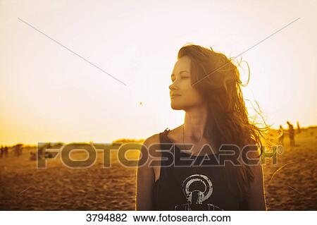 Stock Image - Portrait of a young woman in profile, on the beach Praia do Barril in a sunset, deTavira city, region of Algarve, Portugal. Fotosearch