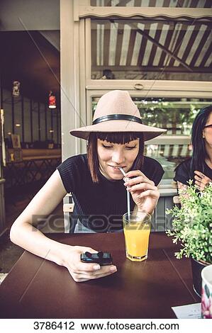 Portrait of a young woman sitting in a restaurant terrace, consultant mobile phone, drinking fruit juice View Large Photo Image Stock Image - Portrait of a young woman sitting in a restaurant terrace, consultant mobile phone, drinking fruit juice. Fotosearch