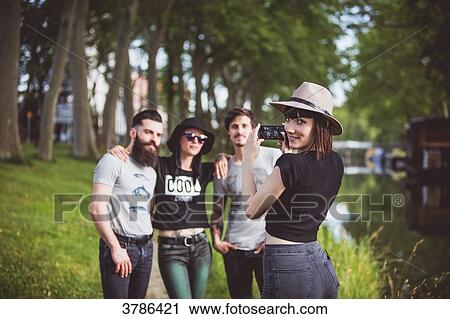 Stock Image - Portrait of a young woman taking pictures of these friends on the banks of the Garonne, barges in the background. Fotosearch