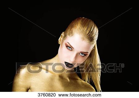 Stock Image - Portrait of a young woman, the body painted in gold, head down, eyes open. Fotosearch