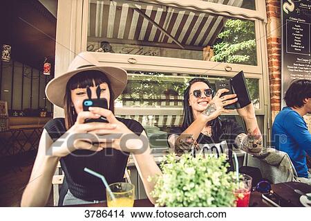 portrait of two young women sitting in a restaurant terrace, taking selfies View Large Photo Image Picture - portrait of two young women sitting in a restaurant terrace, taking selfies. Fotosearch