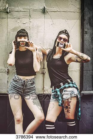 Portrait of two young women, the phone in front of the mouth in front of a wooden wall View Large Photo Image Picture - Portrait of two young women, the phone in front of the mouth in front of a wooden wall. Fotosearch