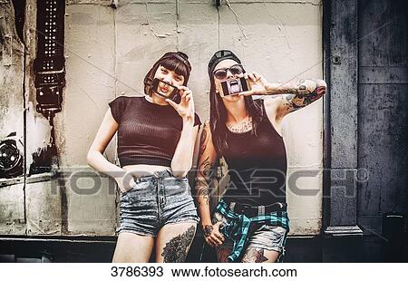 Portrait of two young women, the phone in front of the mouth in front of a wooden wall View Large Photo Image Stock Image - Portrait of two young women, the phone in front of the mouth in front of a wooden wall. Fotosearch