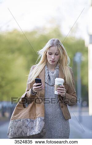 Pretty blonde woman checking her mobile with coffee to go walking in city center View Large Photo Image Stock Photography - Pretty blonde woman checking her mobile with coffee to go walking in city center. Fotosearch