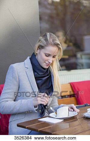 Picture - Pretty blonde woman enjoying a cake and coffee in city center. Fotosearch