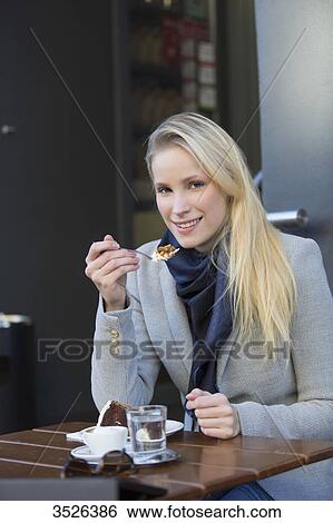 Pretty blonde woman enjoying a cake and coffee in city center looking at camera View Large Photo Image Stock Photograph - Pretty blonde woman enjoying a cake and coffee in city center looking at camera. Fotosearch