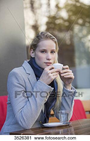Stock Image - Pretty blonde woman enjoying a cup of coffee in a Cafe and looking at camera. Fotosearch