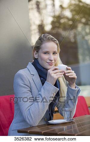 Stock Image - Pretty blonde woman enjoying a cup of coffee in a Cafe and smiling at camera. Fotosearch